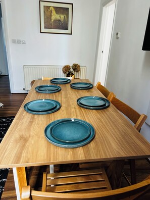 A dining table with six blue plates, wooden chairs, a framed picture on the wall, and a radiator below.