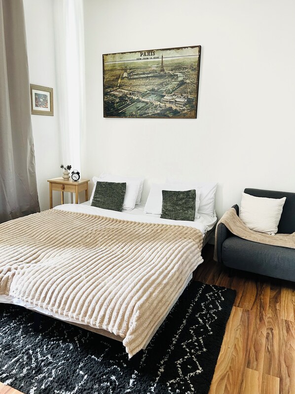 A bedroom with a bed, bedside table, and a painting of Paris.