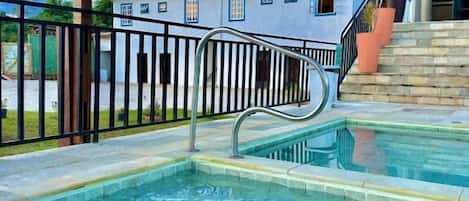 A swimming pool with a metal ladder and a large umbrella.