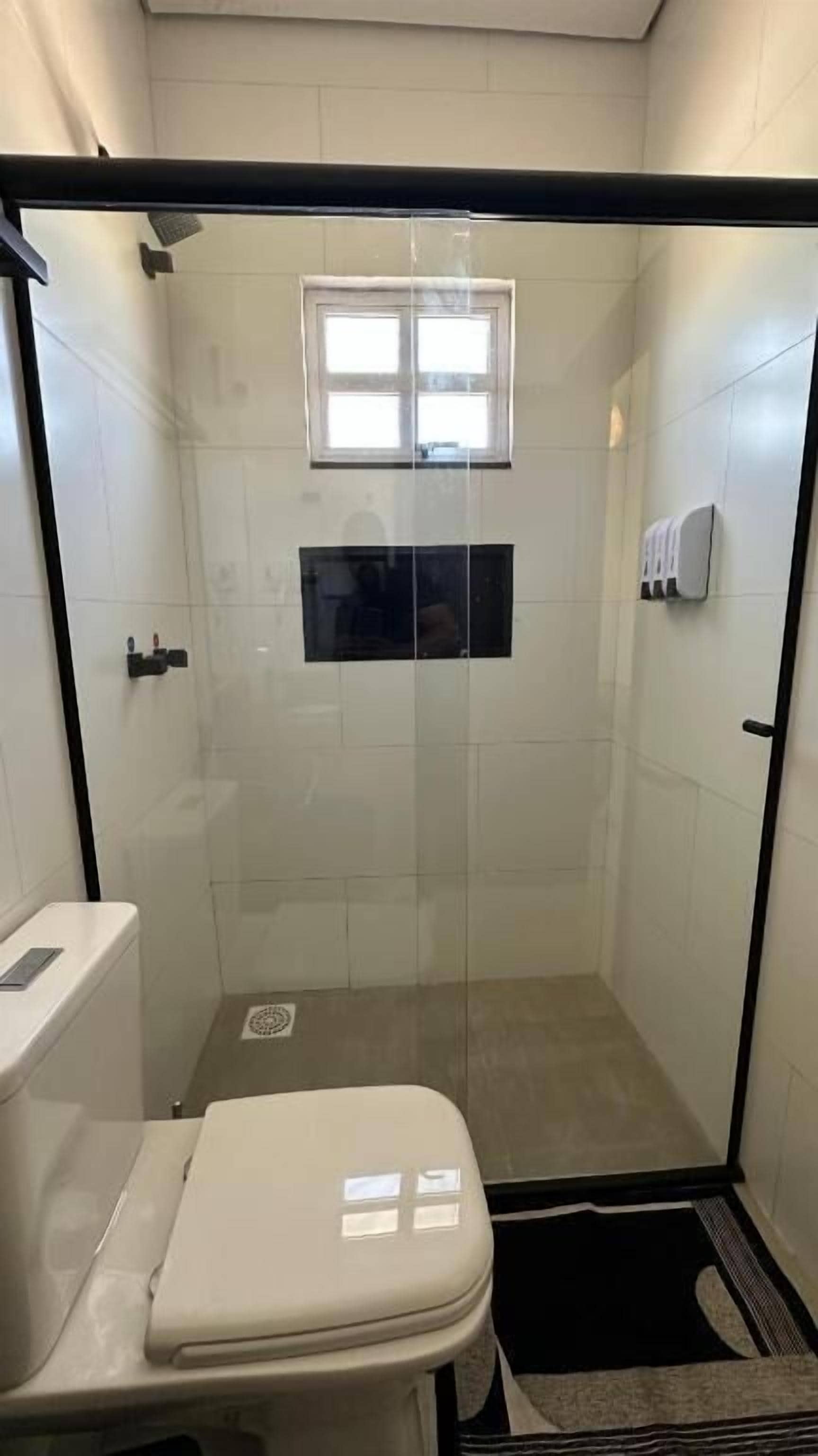 A small, enclosed shower stall with a toilet and a window.