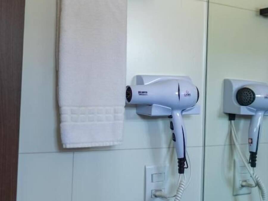 Un baño con dos secadores de pelo fijados a la pared, una toalla colgada en un perchero y un espejo que refleja la habitación.