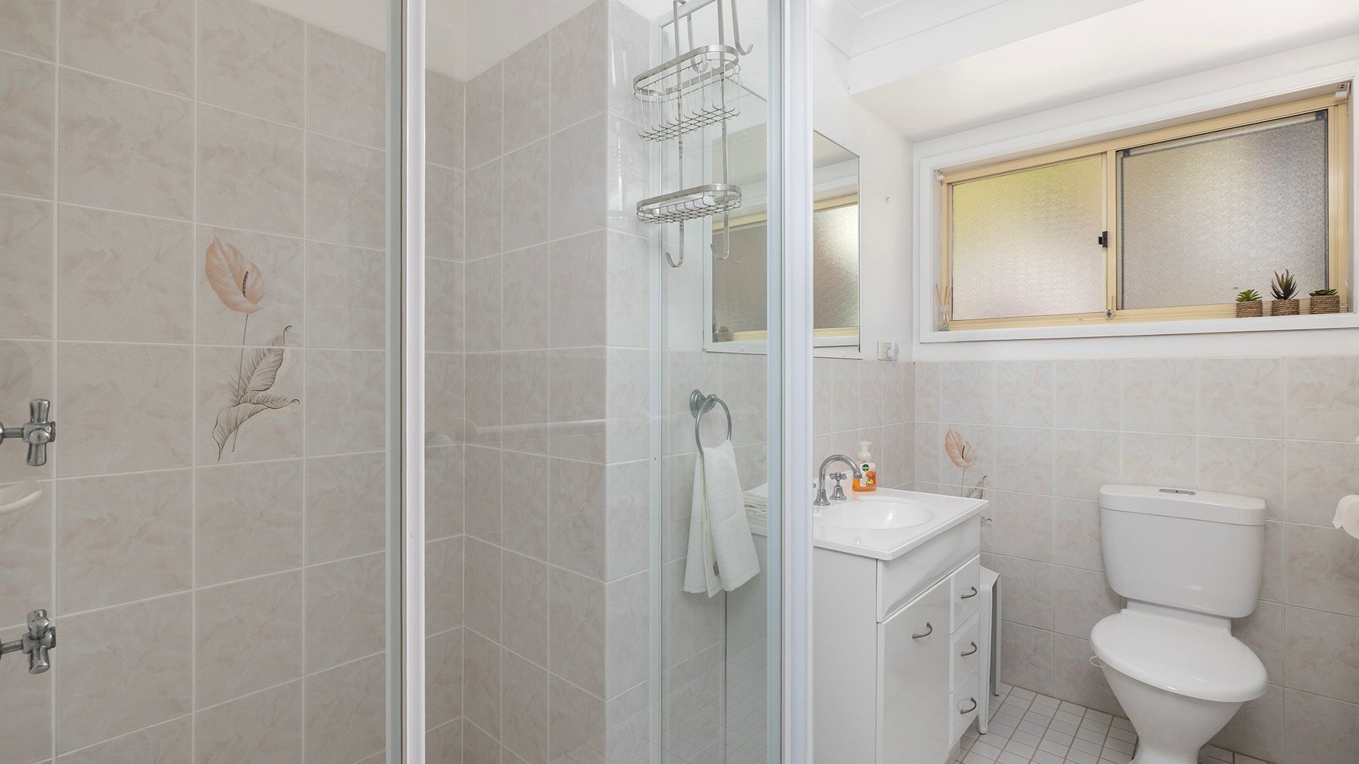 A bathroom with a glass-enclosed shower, a toilet, a sink, and a window above the sink.
