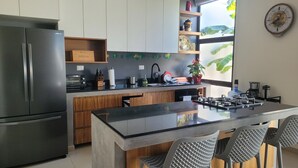 A modern kitchen with a stainless steel refrigerator, wooden cabinets, a built-in oven, and a large island with bar stools. - Private Escape w/ Pool in Sunny Mexico (Conkal Xcuyum)