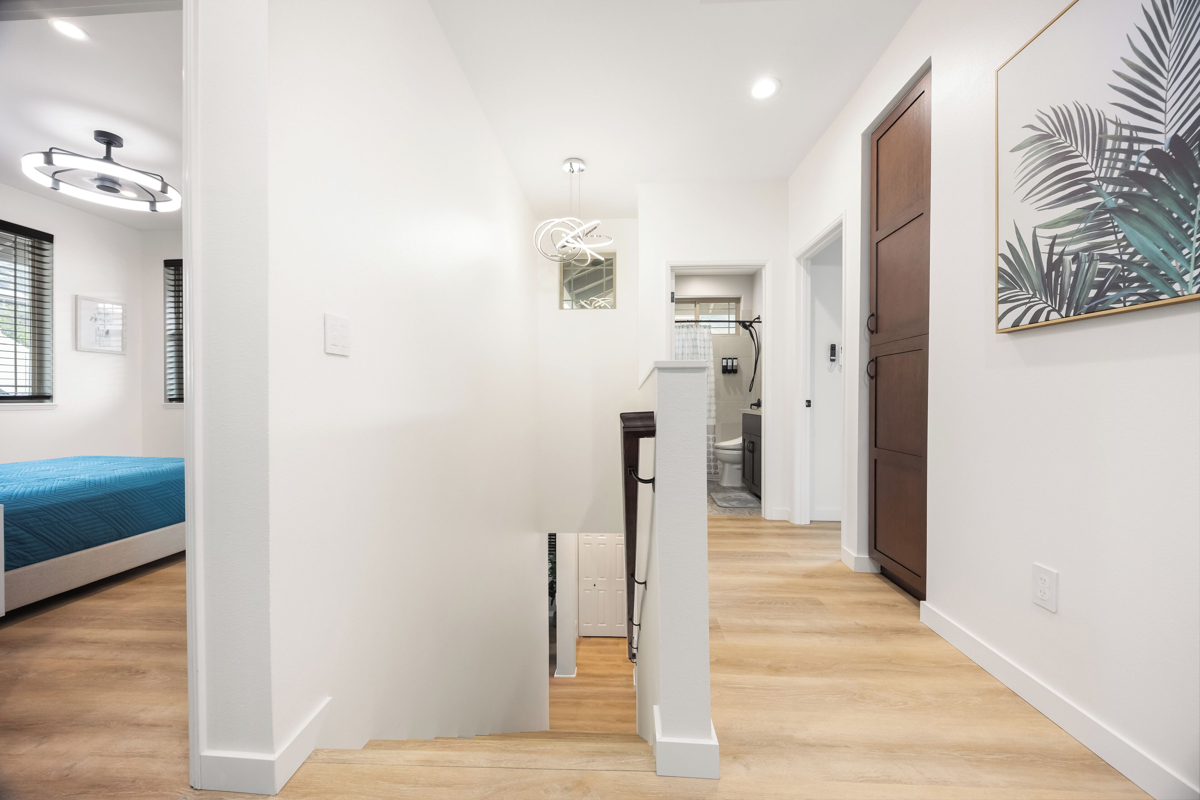 A modern, well-lit hallway with a staircase leading to a bedroom with a blue bed.