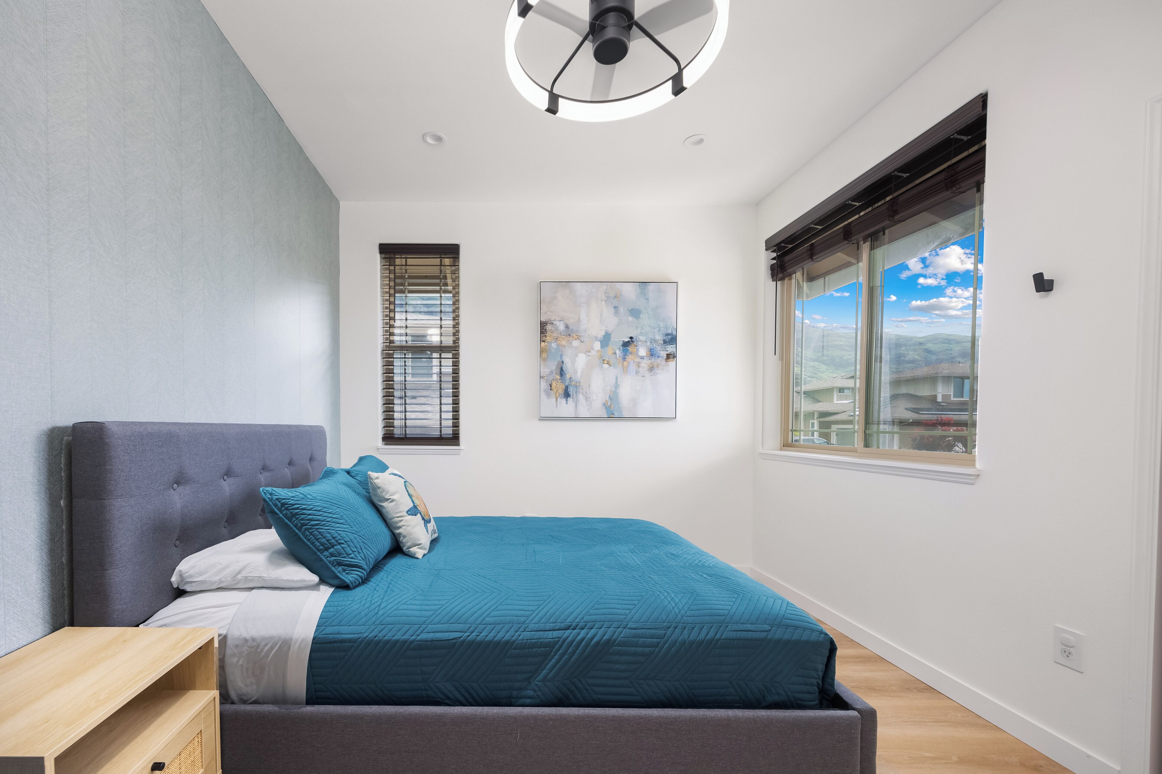 Un dormitorio moderno con una cama grande, una mesita de noche, un ventilador de techo, una ventana con persianas y un cuadro en la pared.