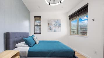 Un dormitorio moderno con una cama grande, una mesita de noche, un ventilador de techo, una ventana con persianas y un cuadro en la pared.
