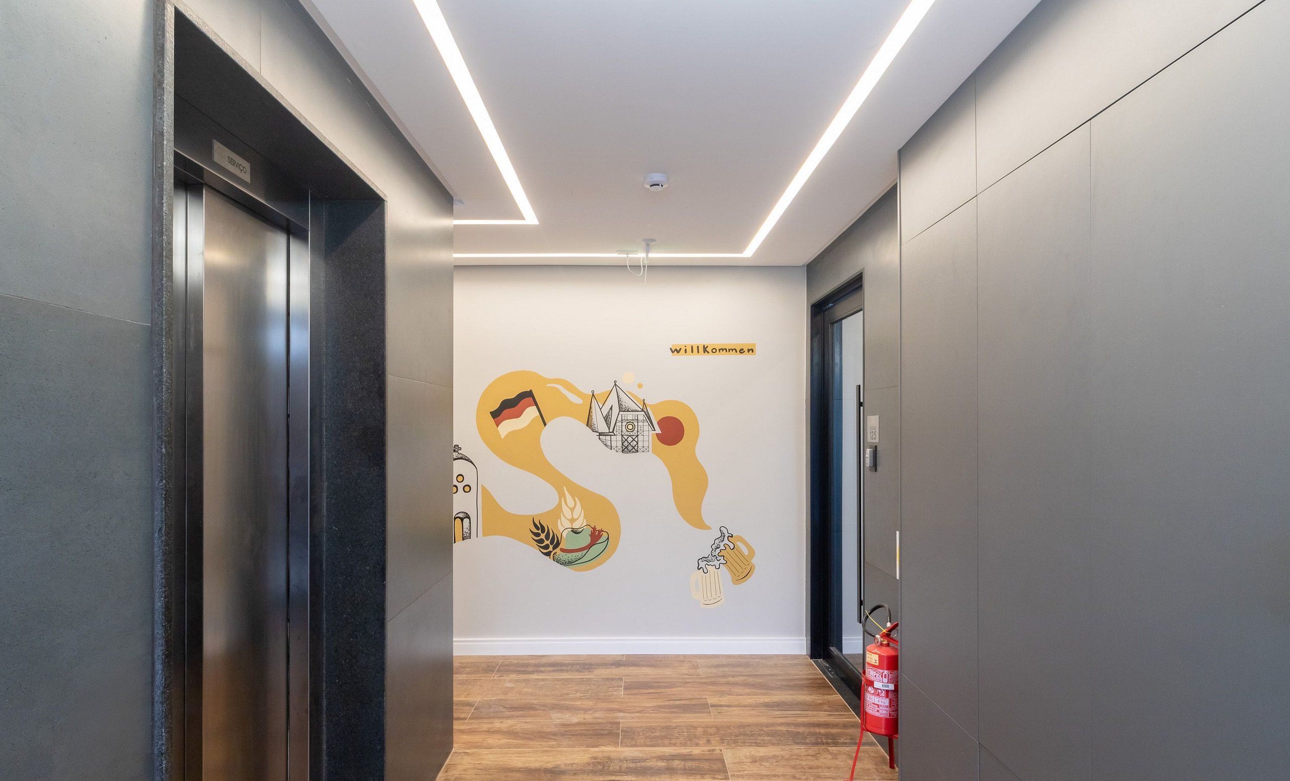 A modern hallway with a wooden floor, a fire extinguisher, and a welcome sign on the wall.