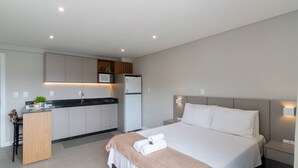 A modern hotel room with a bed, bedside tables, a desk, and a kitchenette. - Your Exclusive Stay in Blumenau, 350m From Vila Germanica - Ocns (Blumenau)