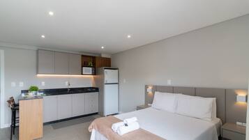 A modern hotel room with a bed, bedside tables, a desk, and a kitchenette.