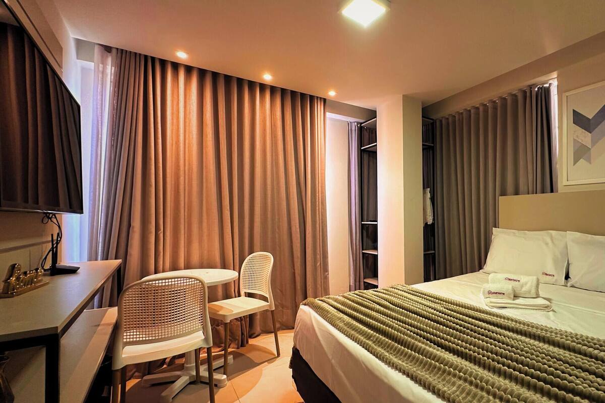A hotel room with a bed, a desk with a chair, a television, and a wardrobe.