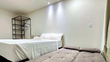 Quarto com cama, mesa de cabeceira, prateleira suspensa e tomada na parede.