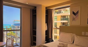 A hotel room with a bed, a chair, a window with a view of the sea, and a balcony. - Vivendas do Mar - LikeHome Hospedagens (João Pessoa)