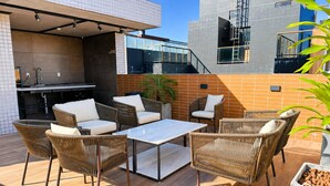 Una terrazza esterna con mobili in vimini, un tavolo con piano in vetro e un angolo cottura integrato.