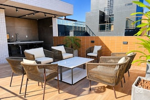An outdoor patio with wicker furniture, a glass-top table, and a built-in kitchen area. - Vivendas do Mar - LikeHome Hospedagens (João Pessoa)