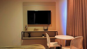 Camera d'albergo con televisione a schermo piatto montata a parete, un tavolino con due sedie e un divano.