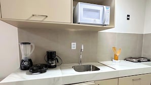 Una cucina con forno a microonde, frullatore, macchina da caffè, lavello e utensili in legno sul ripiano.