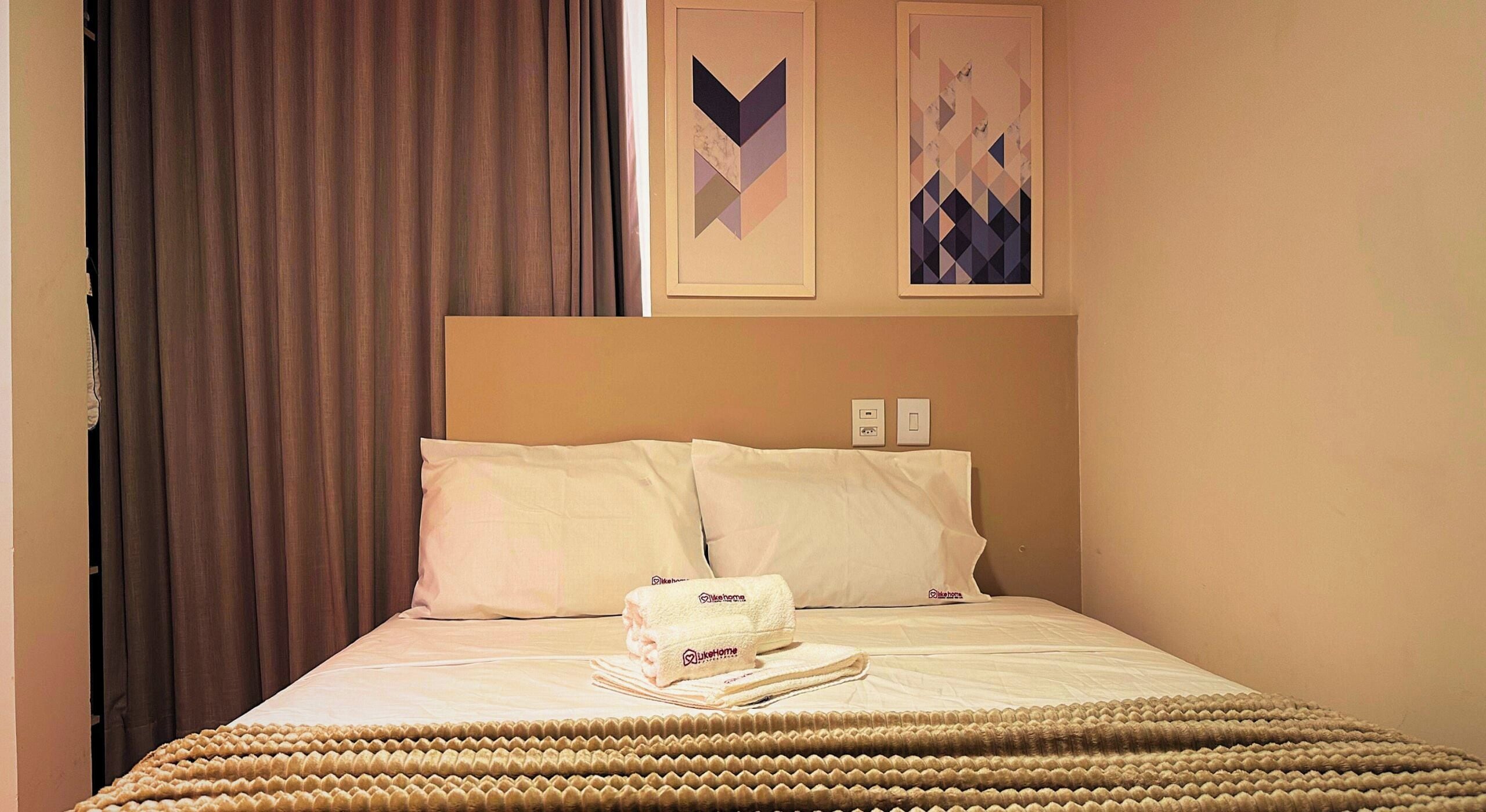 A hotel room with a bed, pillows, a blanket, and a folded towel on the bed.
