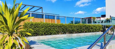 A swimming pool with a metal railing, surrounded by a wooden fence and green hedges.