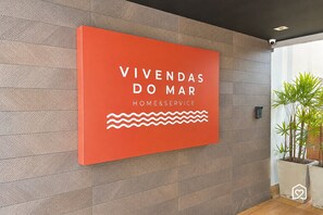 Un letrero con el texto 'VIVENDAS DO MAR HOME&SERVICE' y un diseño de línea ondulada.