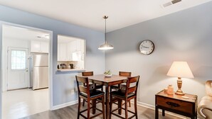 Un comedor con una mesa y sillas de madera, una lámpara colgante, un reloj en la pared y una lámpara en una mesita auxiliar.