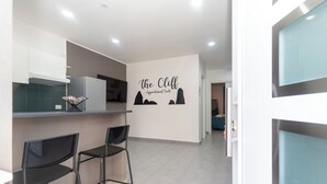 Et moderne køkken med barområde, to sorte barstole og en væg med skiltet 'The Cliff Apartment Suite'.