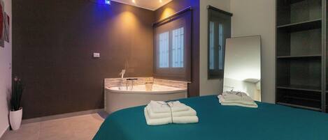 A modern bathroom with a bathtub, a sink, and a large mirror. There are towels on the bed and a potted plant in the corner.