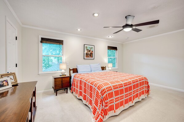 A bedroom with a bed, two windows, a ceiling fan, and a nightstand with a lamp.