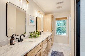 A bathroom with two sinks, a large mirror, wooden cabinets, and a window with a view of trees.