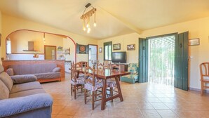 A spacious living area with a dining table and chairs, a sofa, a television, and a kitchen in the background. - Casa Rural Los Conde Guadalcanal by Ruralidays (Sevilla)