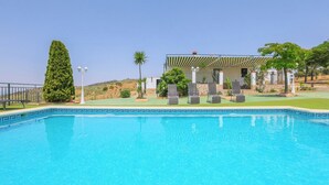A swimming pool with a checkered roof structure, surrounded by lounge chairs and a well-maintained lawn. - Casa Rural Los Conde Guadalcanal by Ruralidays (Sevilla)