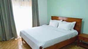 Un lit bien fait, avec une tête de lit en bois, dans une pièce aux murs de couleur claire et au plancher en bois.