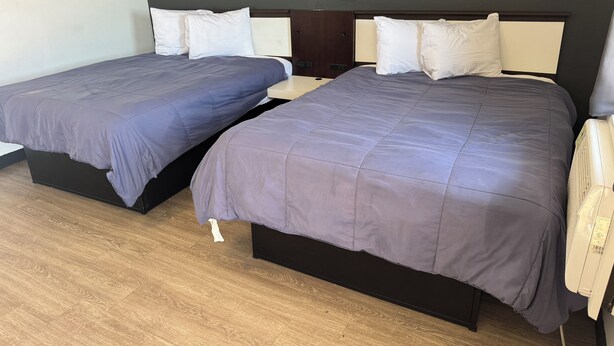 Two beds with dark bedding, a wooden floor, and a wall-mounted heater. - Classic Inn Motel (Temple)