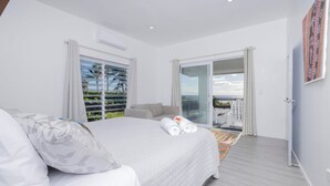 A bedroom with a large bed, a balcony with a view, and a sliding glass door.
