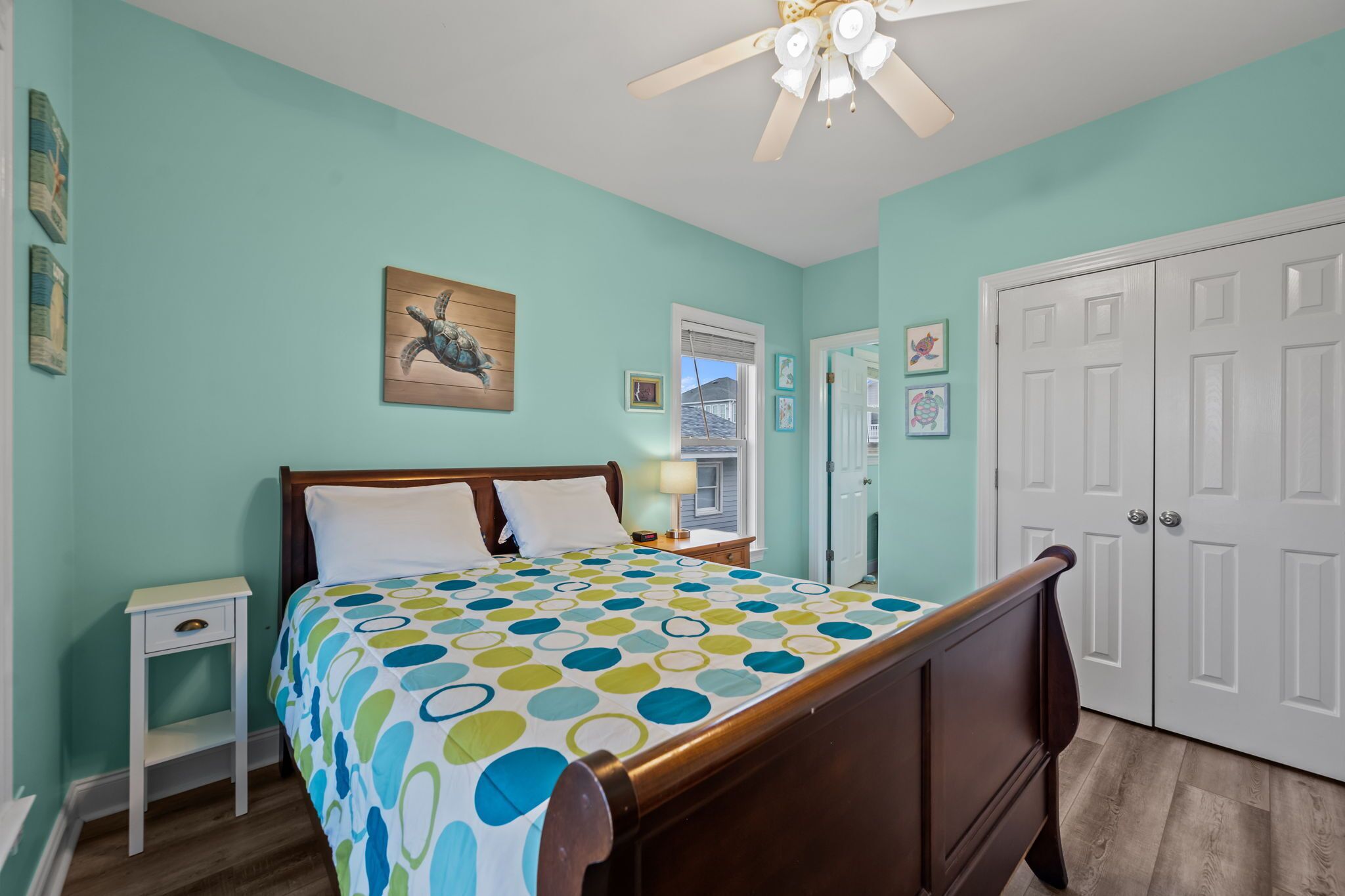 A bedroom with a bed, a nightstand, a ceiling fan, and a door.