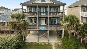Ein zweistöckiges Strandhaus mit Balkon, einer kleinen Veranda und Blick auf den Ozean.