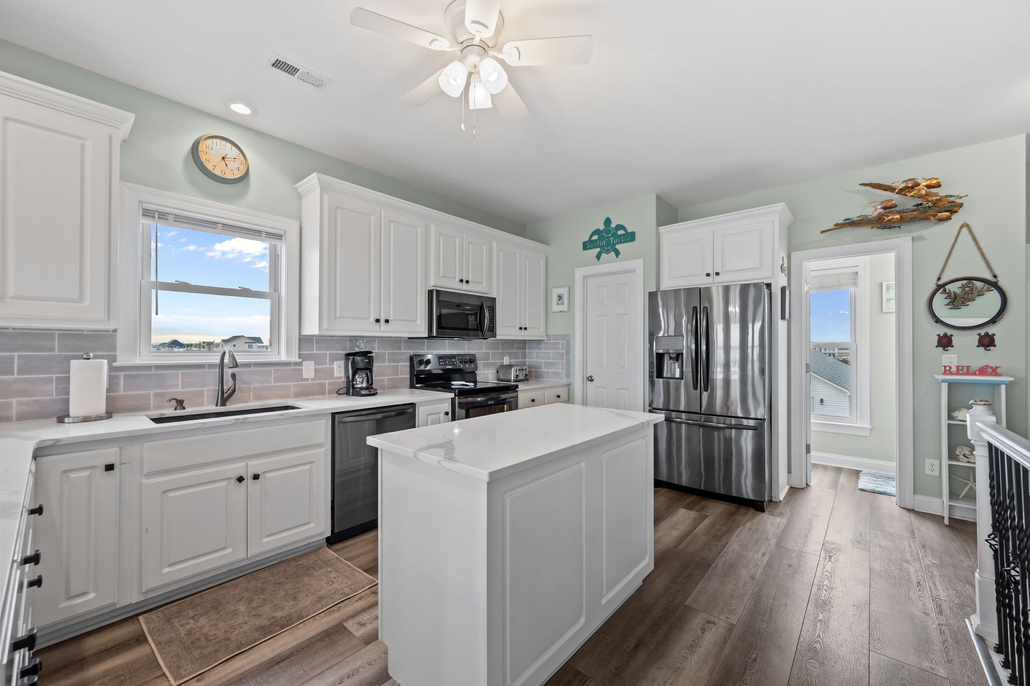 A modern kitchen with white cabinetry, stainless steel appliances, and a large island.