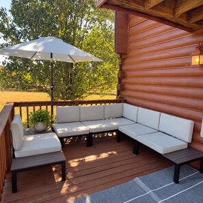 A wooden deck with a built-in white cushioned bench and a table, an umbrella, and a potted plant. - 3-bedroom cabin in peaceful Lascassas with AC (Lascassas)