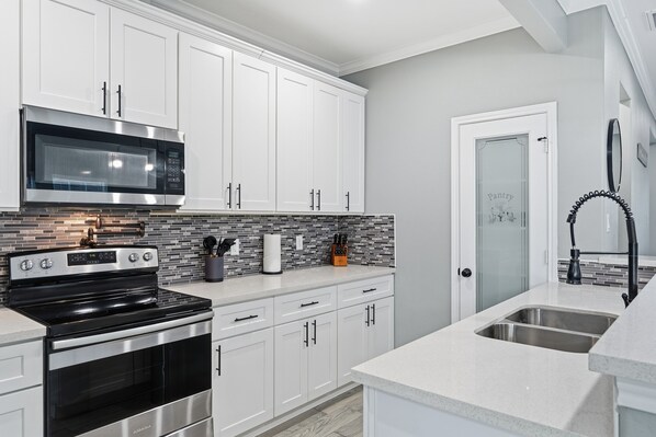 A modern kitchen with white cabinets, a stainless steel stove, a microwave, and a tiled backsplash.