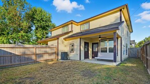 A two-story house with a covered porch, a fenced backyard, and a large tree in the background. - NRG Rest & Rally | Sleeps 12 (Houston)