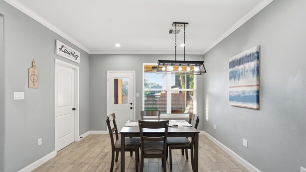 A dining area with a table and chairs, a ceiling light fixture, and a door with a sign. - NRG Rest & Rally | Sleeps 12 (Houston)