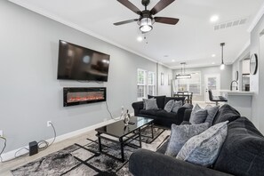 A modern living room with a flat-screen TV, fireplace, ceiling fan, and a dining area with a table and chairs. - NRG Rest & Rally | Sleeps 12 (Houston)