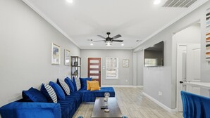 A living room with a blue sectional sofa, a coffee table, and a ceiling fan. - NRG Rest & Rally | Sleeps 12 (Houston)