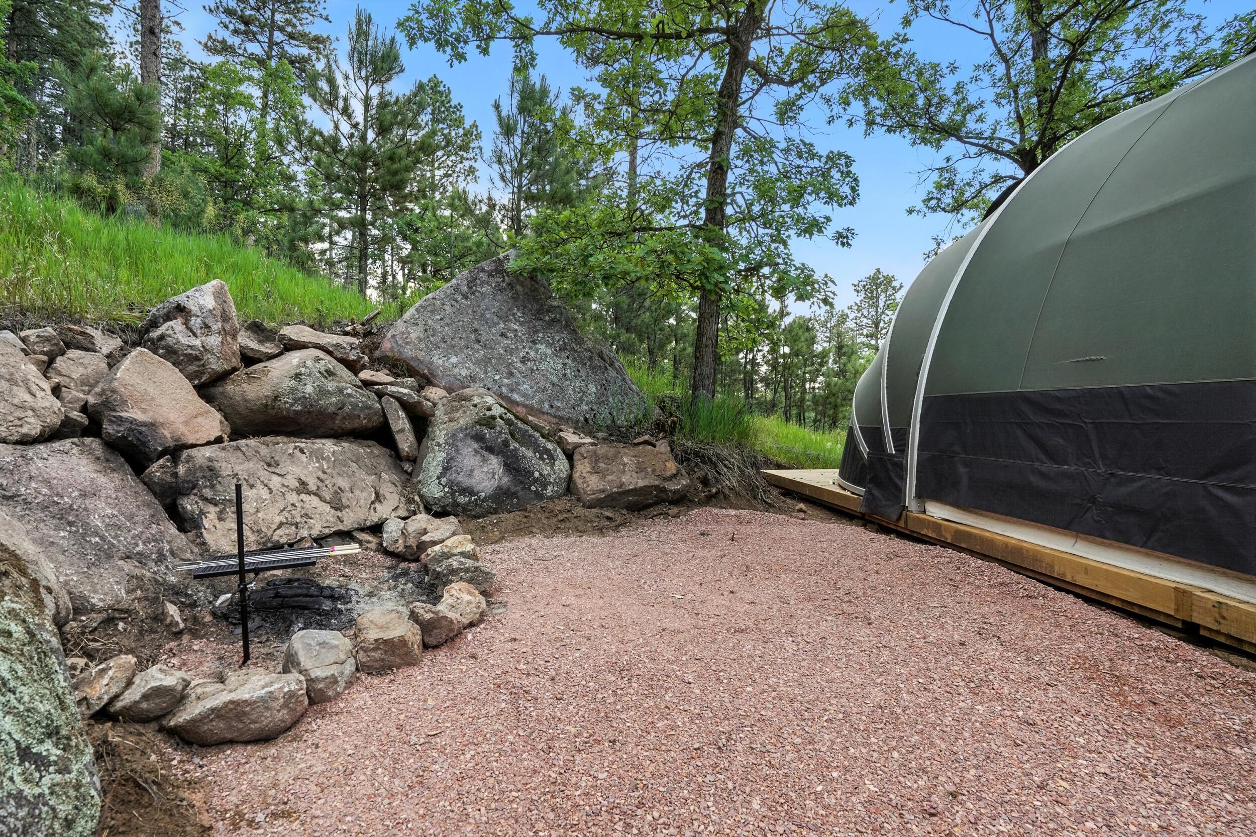 A tent set up next to a stone wall with a gravel path leading to it.