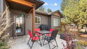 Une terrasse avec une table et des chaises, un barbecue et une maison avec une porte et des fenêtres.