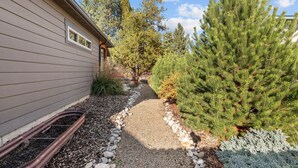 Un chemin menant à une maison bordée d’une allée de gravier et entourée d’arbres à feuilles persistantes.