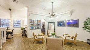Un vaste salon doté d’un plancher en bois, un coin repas avec une table et des chaises, et une cuisine à l’arrière-plan.