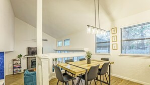 Un espace de repas moderne, avec une table et des chaises en bois, un luminaire suspendu et une vue sur l’extérieur grâce à de grandes fenêtres.