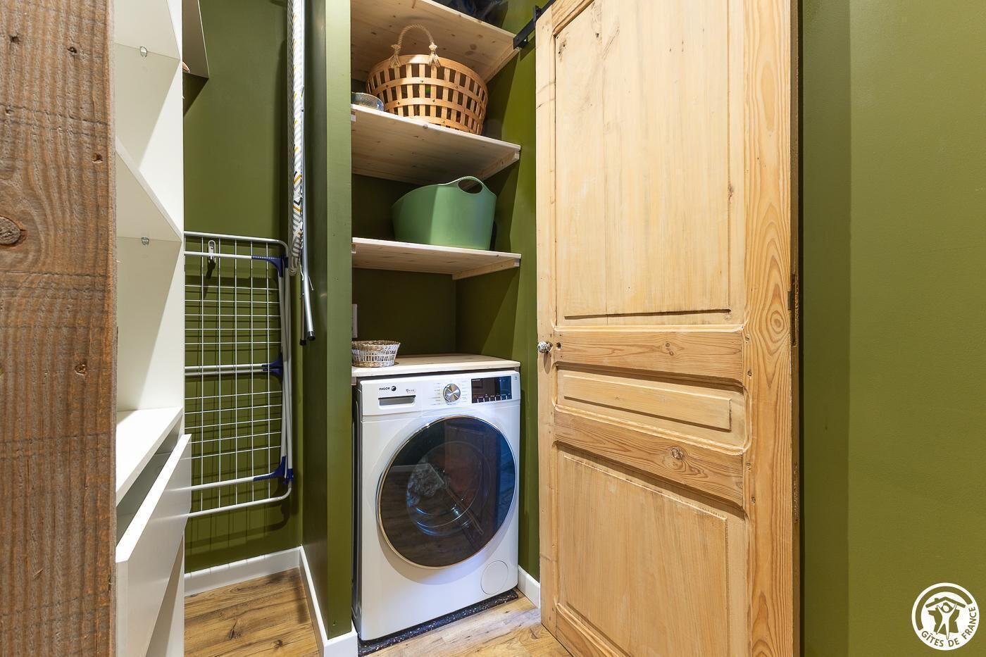 A compact laundry room with a washing machine, shelves, and a wooden cabinet.