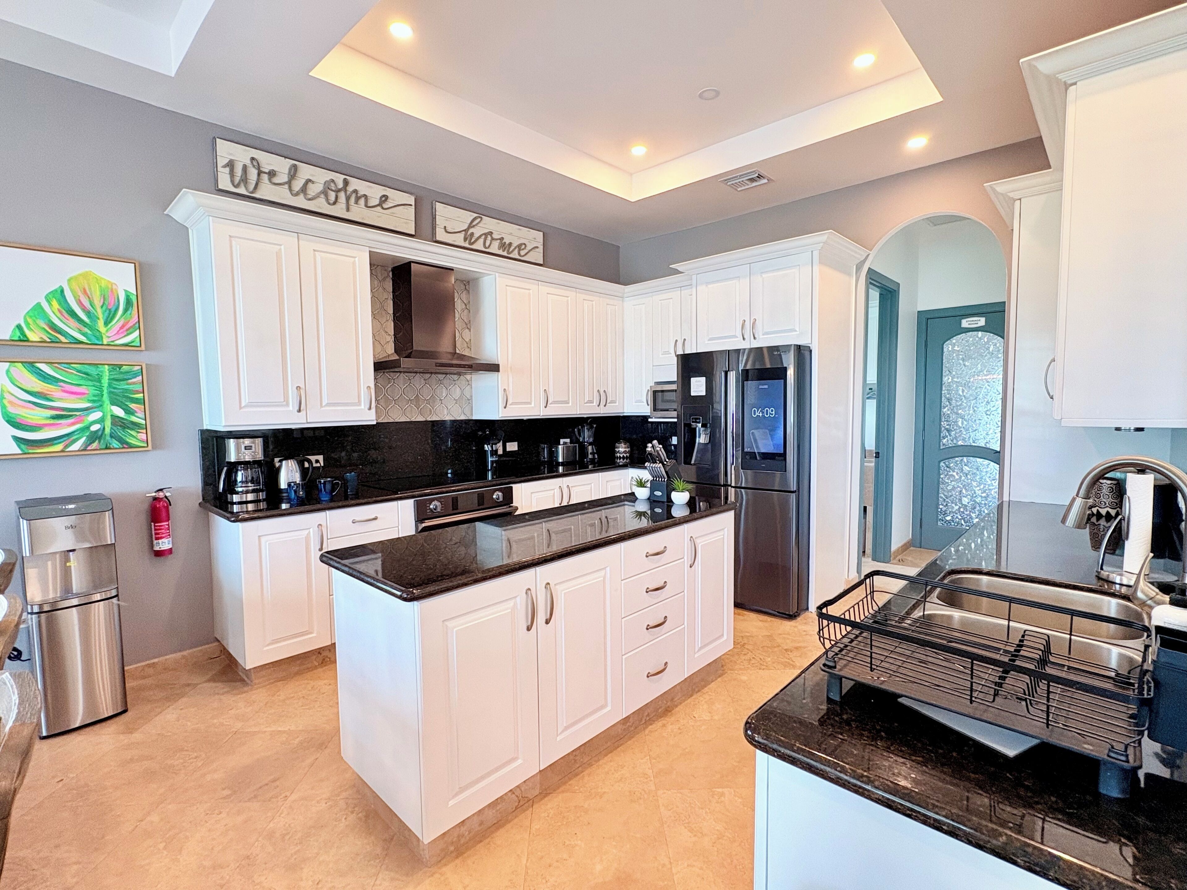 A modern kitchen with white cabinets, a black countertop, stainless steel appliances, and a 'Welcome home' sign.