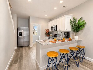 A modern kitchen with a central island, bar stools, and a refrigerator.